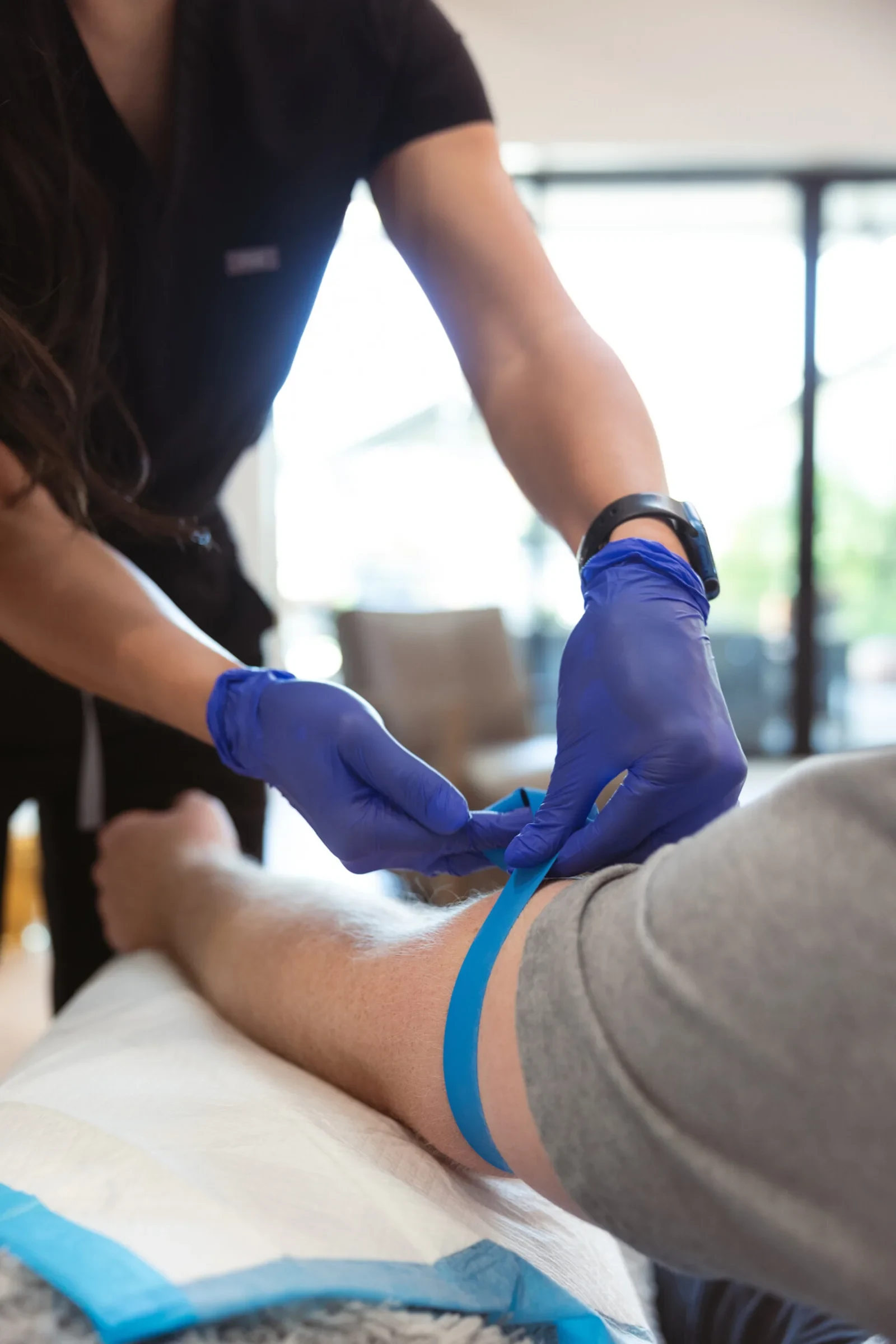 A nurse in blue gloves fitting a tourniquet and prepping a client's forearm on a protective pad before the line goes in