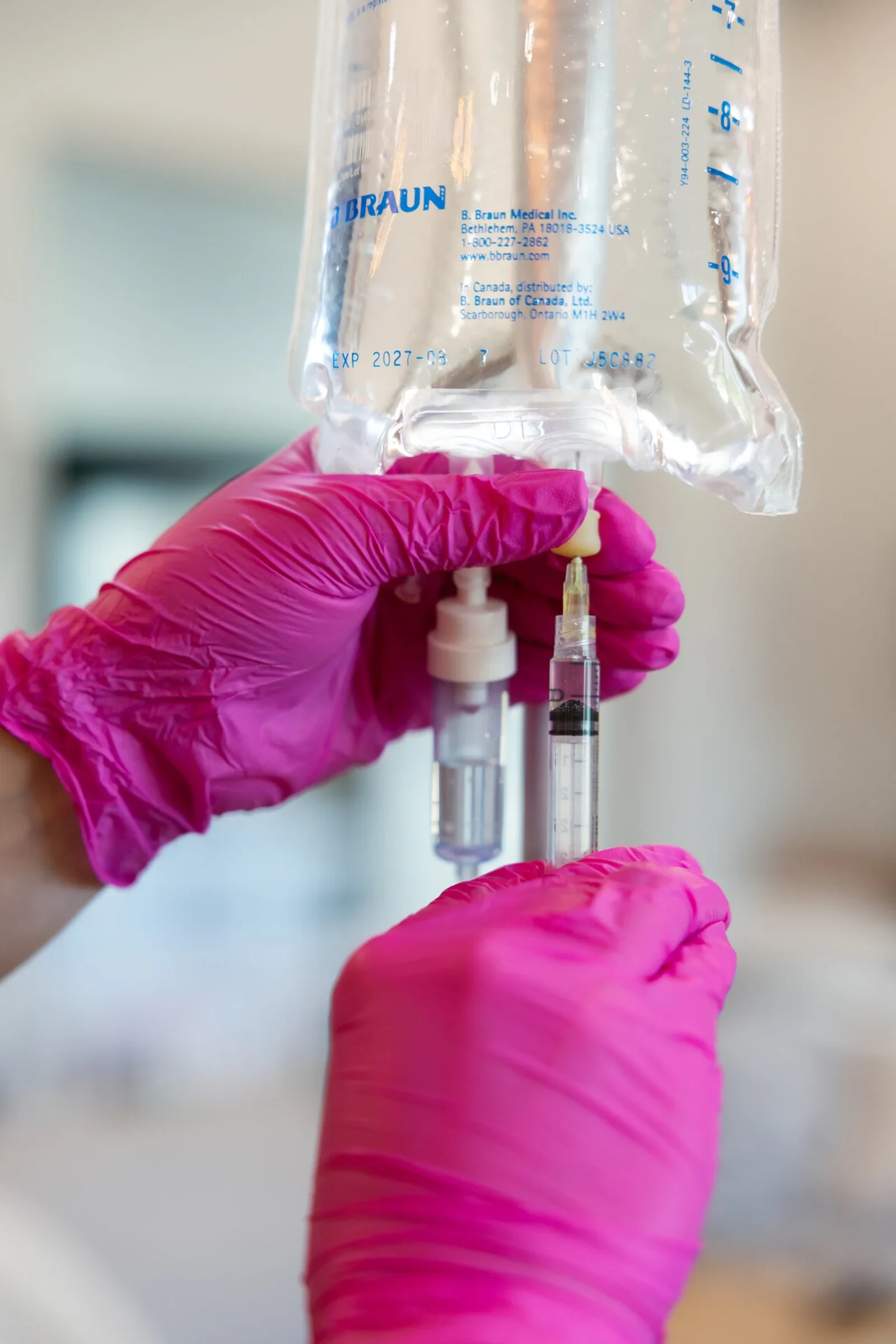 Gloved hands adding vitamin pushes to a one-litre bag before it goes up on the stand