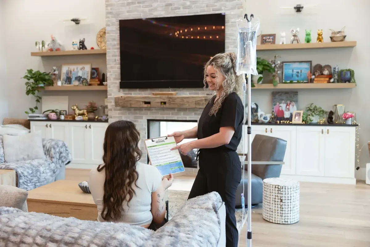 A registered nurse going through the health history with a client seated on her own sofa, the IV stand ready beside them